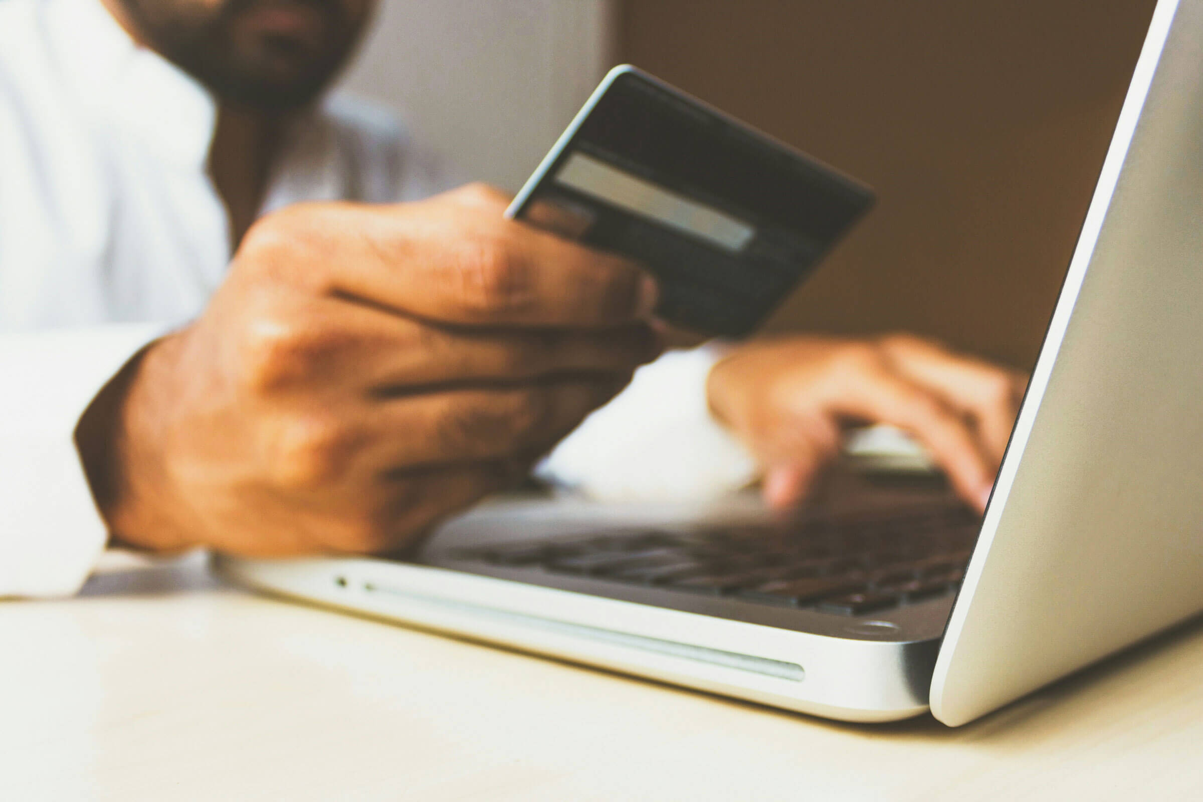 Man holding credit card in front of a laptop computer.