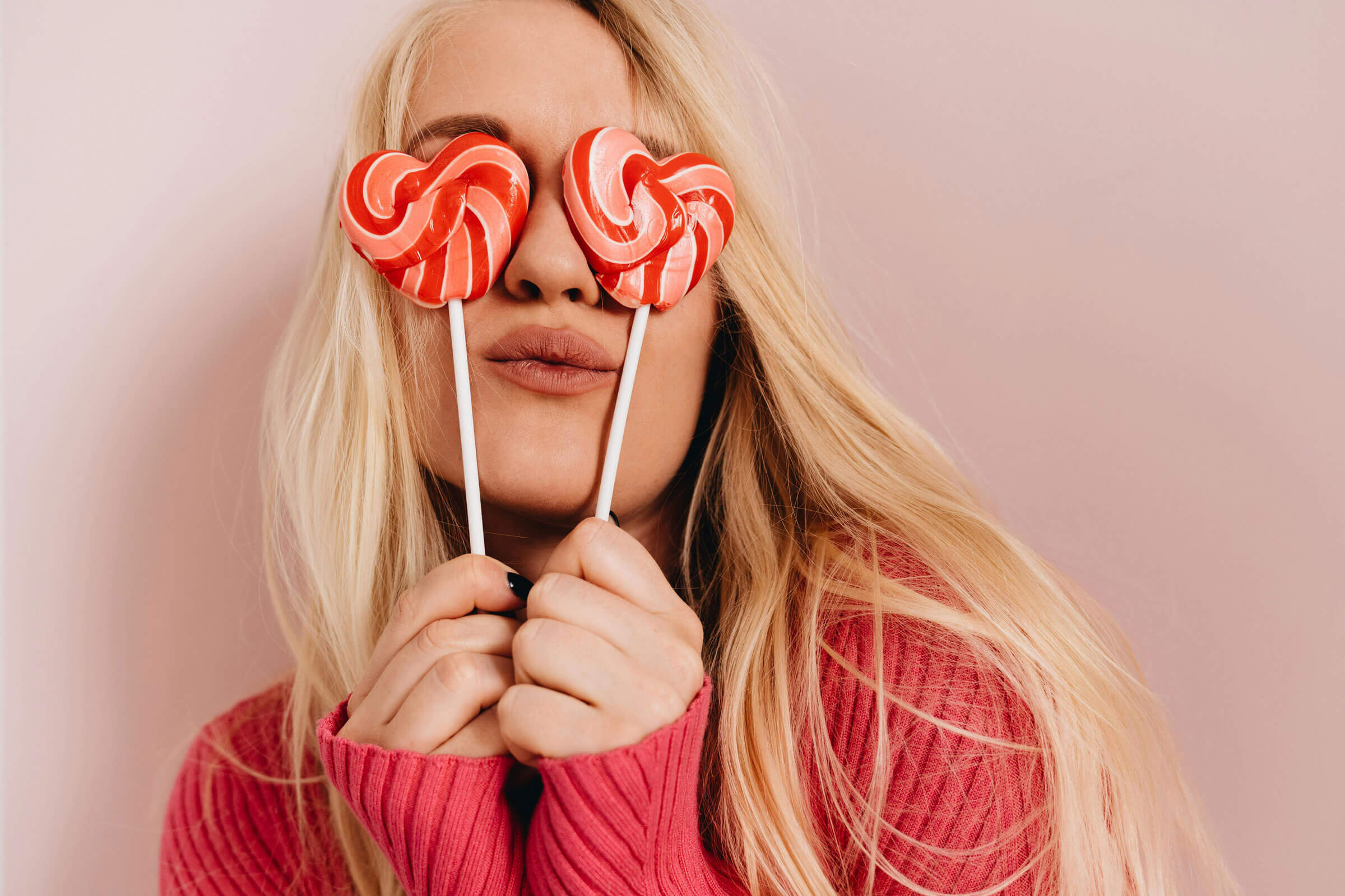 Woman covering each eye with a striped, love heart lollipop.